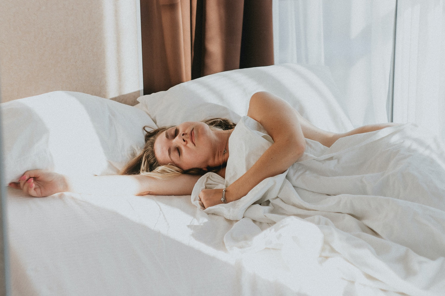 Eine Frau, die in einem Bett liegt mit weißer Bettwäsche.